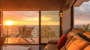 Una stanza con un'ampia porta scorrevole in vetro che dà su un balcone con vista sul tramonto sull'oceano.