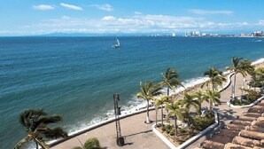 Paesaggio costiero con spiaggia, palme e una barca a vela all'orizzonte.