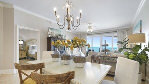 A dining area with a white table, wooden chairs, and a chandelier. There are vases with yellow flowers on the table. - Stunning & Spacious 4BR Beachfront Condo at Adagio B202 with Gulf Front Views! (Santa Rosa Beach)