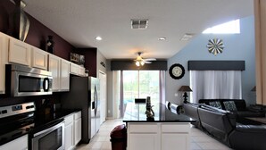 A modern kitchen with white cabinets, stainless steel appliances, and a black countertop. There is a dining area with a black leather sofa and a small table. - Luxury 8 Bedroom Villa, Good for 18 to 20, Pool/Spa (Kissimmee)
