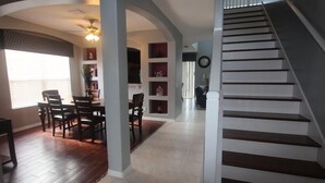 A dining area with a table and chairs, a staircase, and a hallway with shelves. - Luxury 8 Bedroom Villa, Good for 18 to 20, Pool/Spa (Kissimmee)
