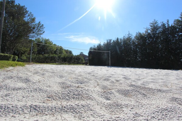A sandy volleyball court with a net, surrounded by trees and a clear sky.
