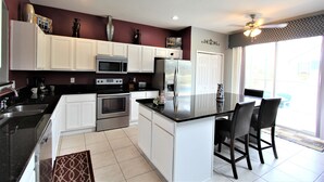 A modern kitchen with white cabinets, stainless steel appliances, and a central island with bar stools. - Luxury 8 Bedroom Villa, Good for 18 to 20, Pool/Spa (Kissimmee)