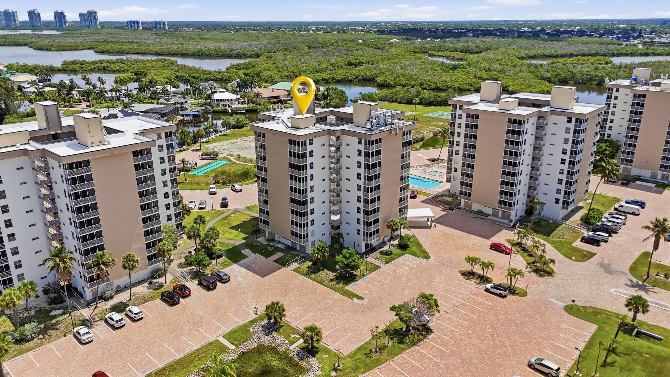 A high-rise residential building complex with multiple parking lots, a swimming pool, and surrounding greenery.