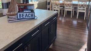 Een keuken met uitzicht op de oceaan, met gestreepte gordijnen, hanglampen en een bordje met de tekst 'BEACH'.
