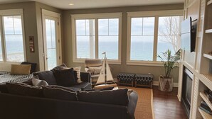 Een woonkamer met een groot raam met uitzicht op de zee, een bank, een stoel en een klein model zeilboot.