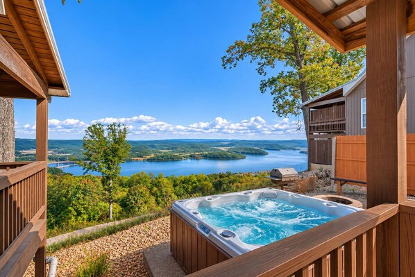 A hot tub on a wooden deck with a view of a lake and mountains.