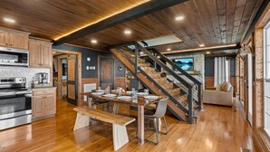 Una cocina amplia con armarios de madera y horno integrado, un comedor con mesa y sillas de madera, y una escalera que lleva a un dormitorio en lo alto.