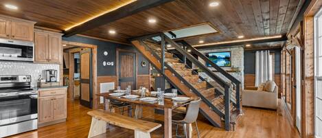 A spacious kitchen with wooden cabinets and a built-in oven, a dining area with a wooden table and chairs, and a staircase leading to a loft bedroom.