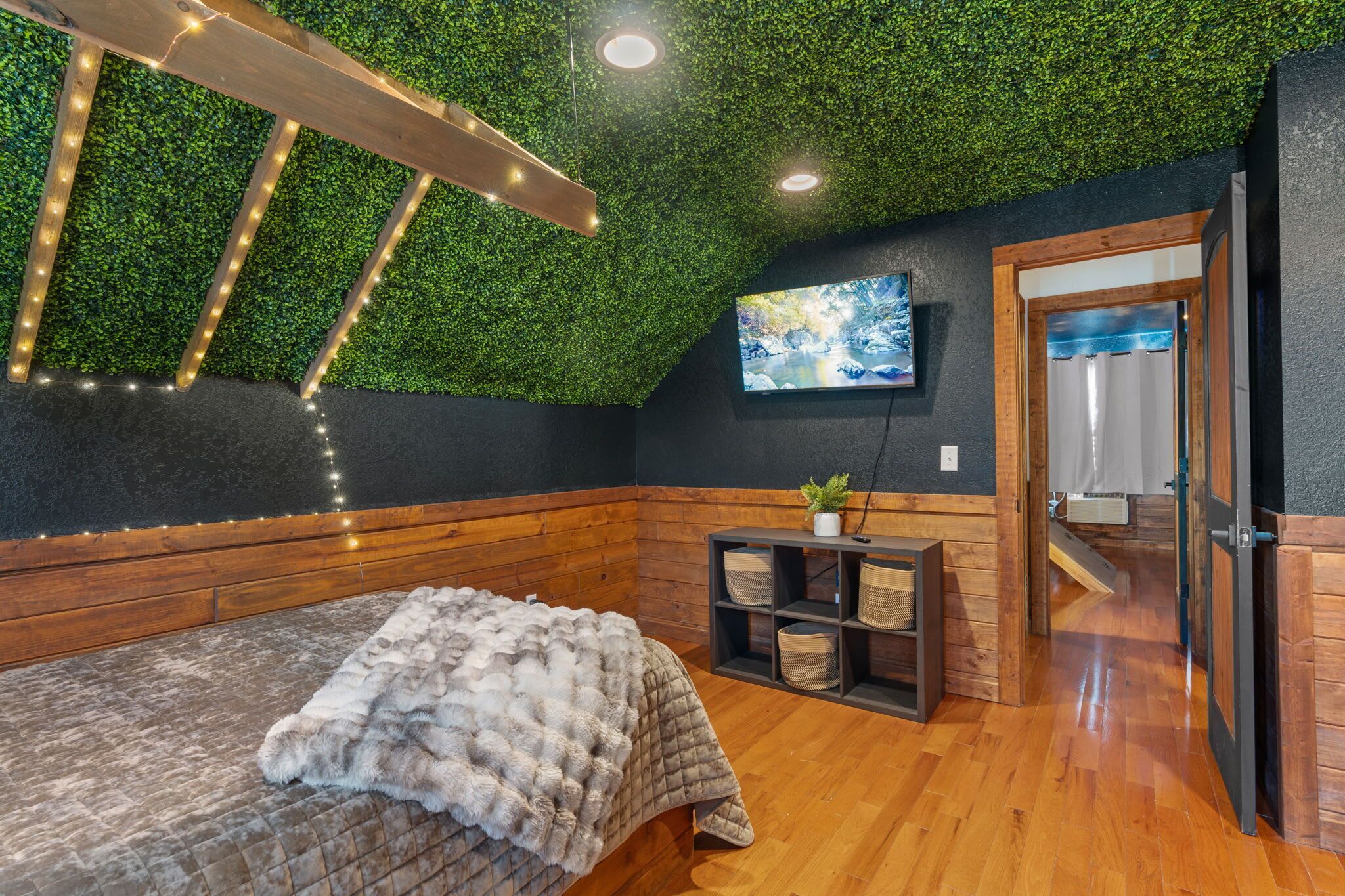 Une pièce chaleureuse avec un banc en bois, un faux plafond vert, un téléviseur fixé au mur et une porte donnant sur une autre pièce.