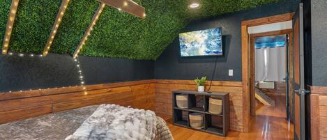 Une pièce chaleureuse avec un banc en bois, un faux plafond vert, un téléviseur fixé au mur et une porte donnant sur une autre pièce.