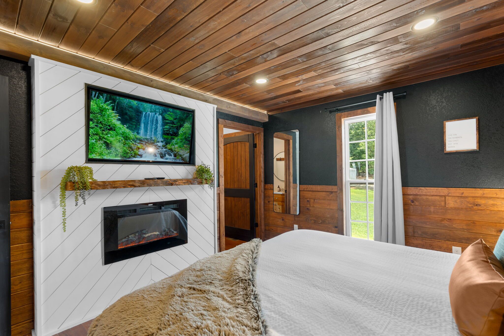 Ein modernes Schlafzimmer mit an der weißen Wand montiertem Fernseher, Kamin und einem großen Bett.