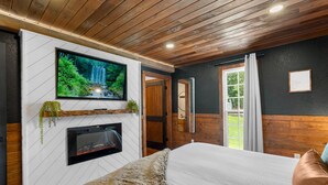 Un dormitorio moderno con una televisión instalada en una pared blanca, una chimenea y una cama grande.