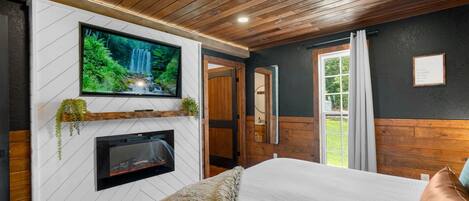 A modern bedroom with a TV mounted on a white wall, a fireplace, and a large bed.