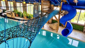 Ein Poolbereich mit Seilbrücke, Rutschen und Holzkonstruktionen.