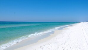 Une vaste plage de sable blanc, bordée d’une eau turquoise et limpide, et surplombée d’un ciel bleu azur.