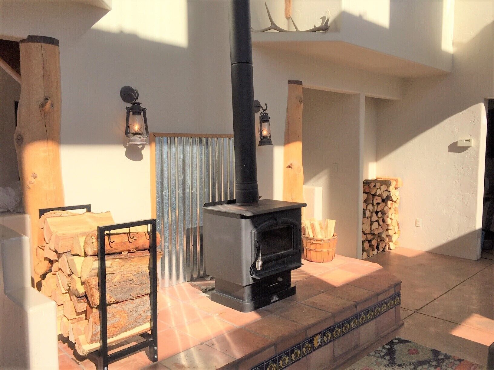 Ein gemütlicher Raum mit Kaminofen, Holzstapel, einem Metallgestell und einer dekorativen Wandverkleidung.