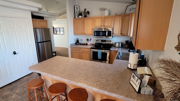 A kitchen with wooden cabinets, stainless steel appliances, a granite countertop, and a bar area with stools. - Green River Mesa…your home away from home! (Green River)