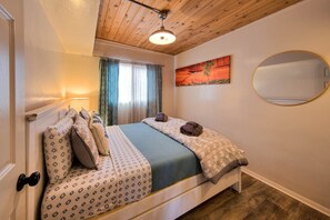 Une chambre avec un plafond en bois, un lit recouvert d’une literie à motifs, un tableau accroché au mur et un miroir rond.