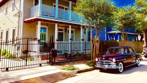 A two-story house with a balcony, a vintage car parked in front, and a wooden fence. - Delightful, Relaxing, Restored Historic Apartment in Montrose section of Houston (Houston)