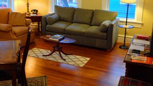 A living room with a green sofa, wooden coffee table, and a ceiling fan. - Delightful, Relaxing, Restored Historic Apartment in Montrose section of Houston (Houston)
