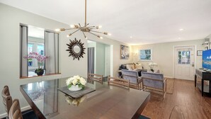 A dining area with a glass table, chairs, and a chandelier. There is a living room with a sofa and a TV. -  ⭐️ Pool & Gulf Views, 2BR + Den,  Prime Siesta Key Location (Sarasota)