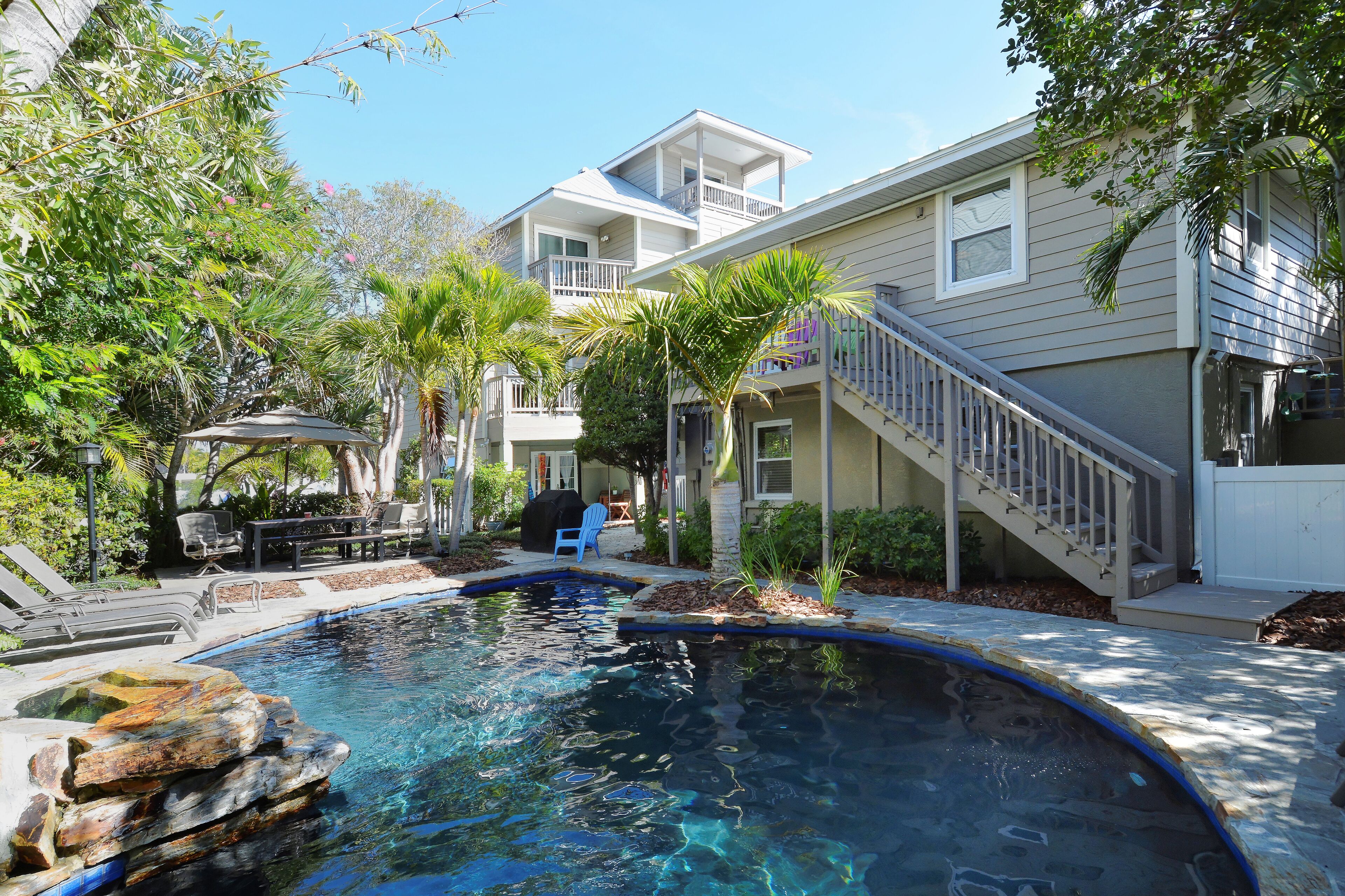 A residential area with a swimming pool, a covered patio, and a staircase leading to a balcony.