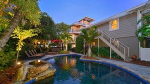 A pool with a stone edge, surrounded by palm trees and lounge chairs. -  ⭐️ Pool & Gulf Views, 2BR + Den,  Prime Siesta Key Location (Sarasota)