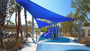 A playground with a slide and climbing structures, surrounded by palm trees and shaded by blue canopies. -  ⭐️ Pool & Gulf Views, 2BR + Den,  Prime Siesta Key Location (Sarasota)