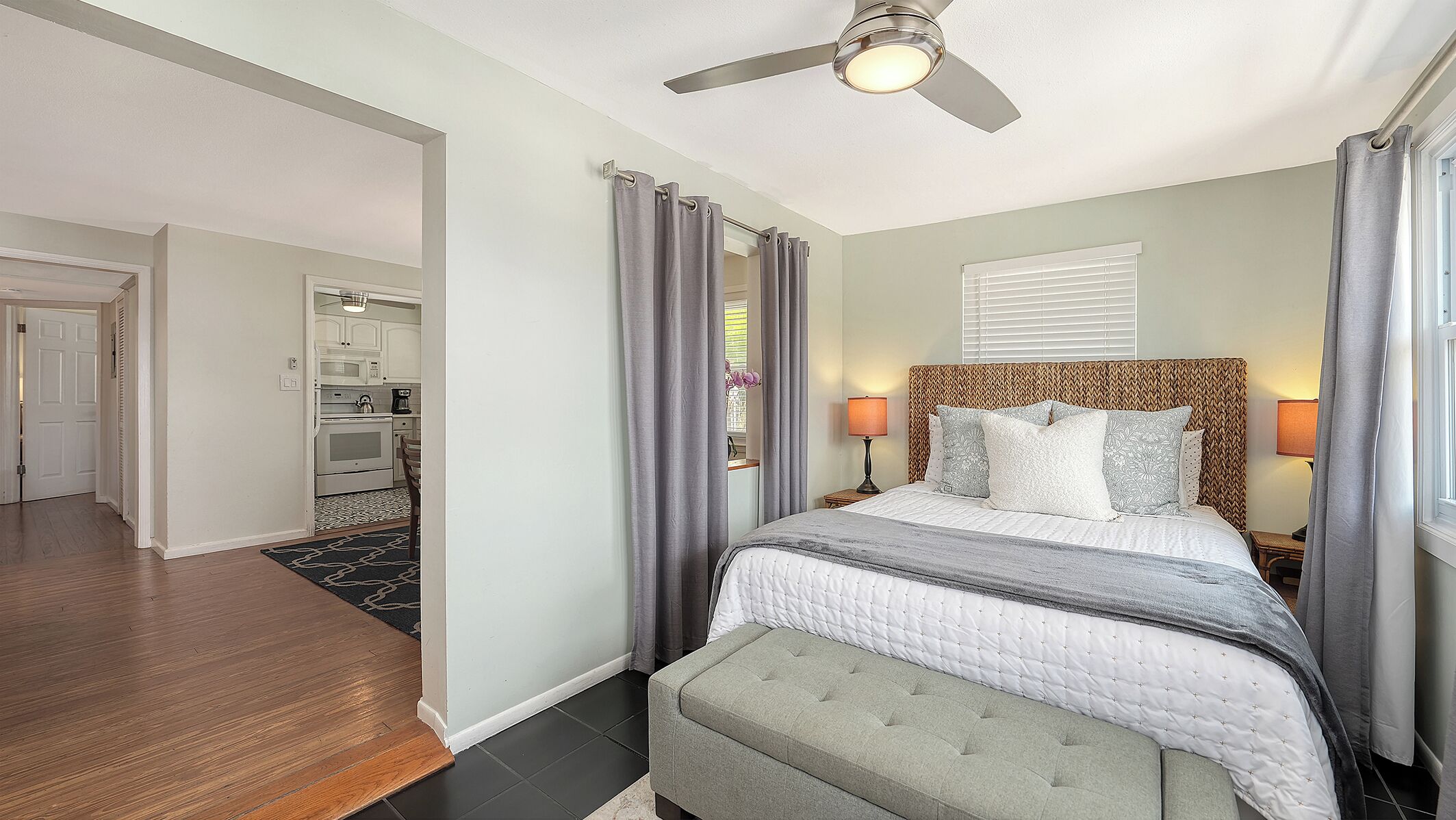 A hotel room with a bed, bedside lamps, a ceiling fan, and a view of the kitchen.