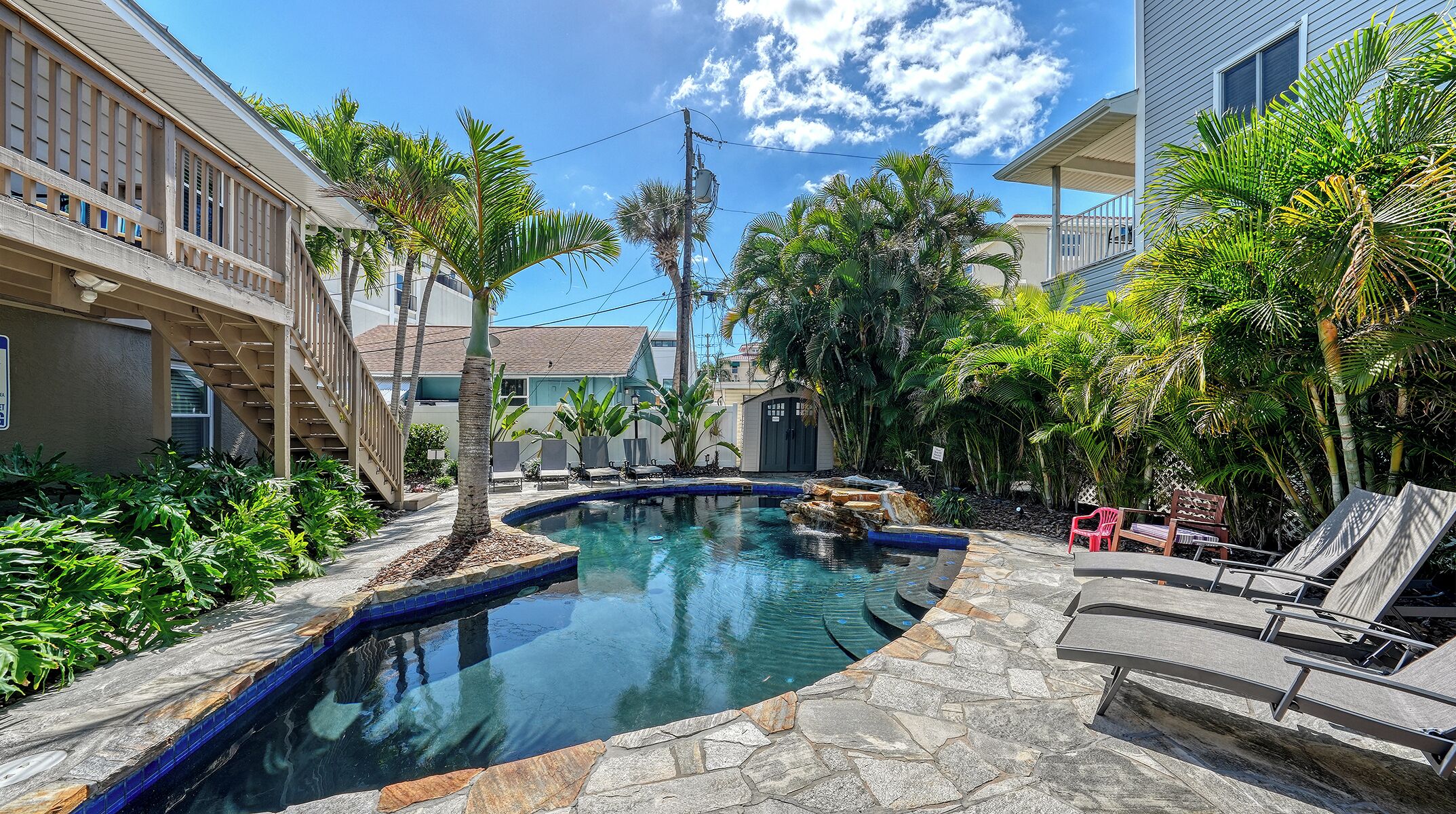 A swimming pool with a stone border, surrounded by palm trees and lounge chairs.