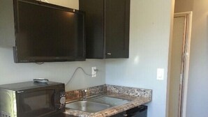 A compact kitchen with dark cabinetry, a microwave, a sink, and a small countertop. - "Tiny Diggs" Is A Very Simple Lifestyle For One! (Jupiter)