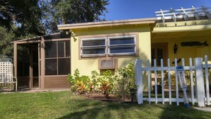 A yellow building with a white picket fence, a covered porch, and a small garden with plants. - "Tiny Diggs" Is A Very Simple Lifestyle For One! (Jupiter)