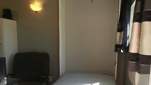 A small, single-bed room with a bed at the center, a desk with a chair to the left, and a wall-mounted light fixture above the bed. - "Tiny Diggs" Is A Very Simple Lifestyle For One! (Jupiter)