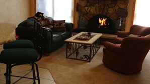 Ein gemütliches Wohnzimmer mit Kamin aus Stein, einer Couch, einem Couchtisch und einem roten Sessel.