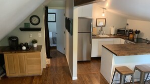 A modern kitchen with wooden flooring, a refrigerator, a microwave, and a sink. There is a wooden counter with stools and a clock on the wall.