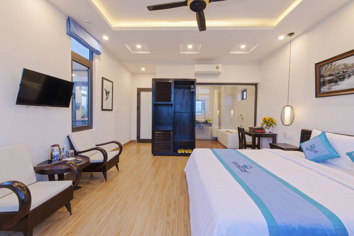 Quarto de hotel com uma cama, uma escrivaninha, uma cadeira, uma televisão e um banheiro visível por uma porta aberta.