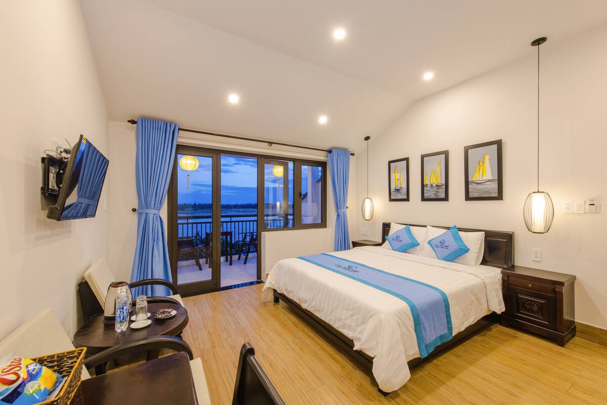 Quarto de hotel com cama, escrivaninha, cadeira, mesa, varanda com vista para o mar e área de jantar.