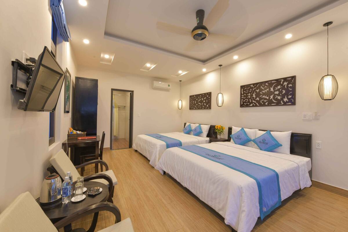 Quarto de hotel com duas camas, uma escrivaninha com cadeira, televisão e ventoinha no teto.