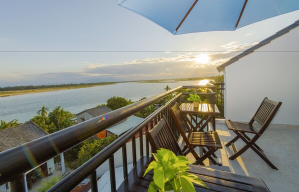 A balcony with a view of a river, wooden furniture, and a potted plant.