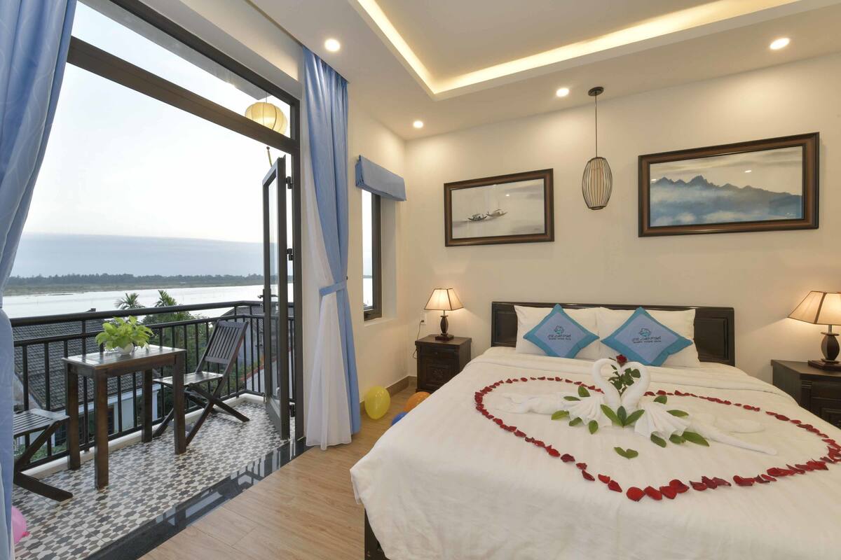Quarto de hotel com varanda, cama decorada com pétalas de rosa e vista para o mar.