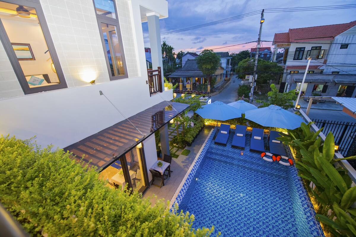 Piscina no terraço com espreguiçadeiras e deck revestido, cercada por áreas verdes e edifícios residenciais.