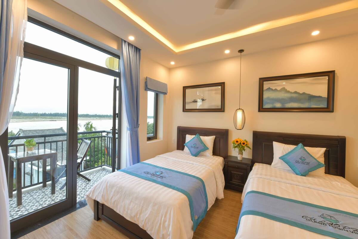 Quarto de hotel com duas camas, varanda e vista para o mar.