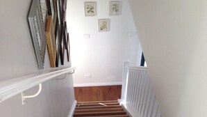 Eine Treppe mit Holzbodenstufen und weißen Geländern, die zu einer Empore mit gerahmten Bildern an der Wand führt.