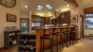 A modern kitchen with a central island, bar stools, wine rack, skylights, and wooden cabinetry. - DOGS, Panoramic Ocean Views, Game Room, EV Charger, New Hot Tub, Chef’s Kitchen (Waldport)