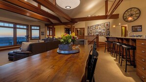 A spacious living area with a wooden dining table, a large window, and a kitchen area with bar stools. - DOGS, Panoramic Ocean Views, Game Room, EV Charger, New Hot Tub, Chef’s Kitchen (Waldport)