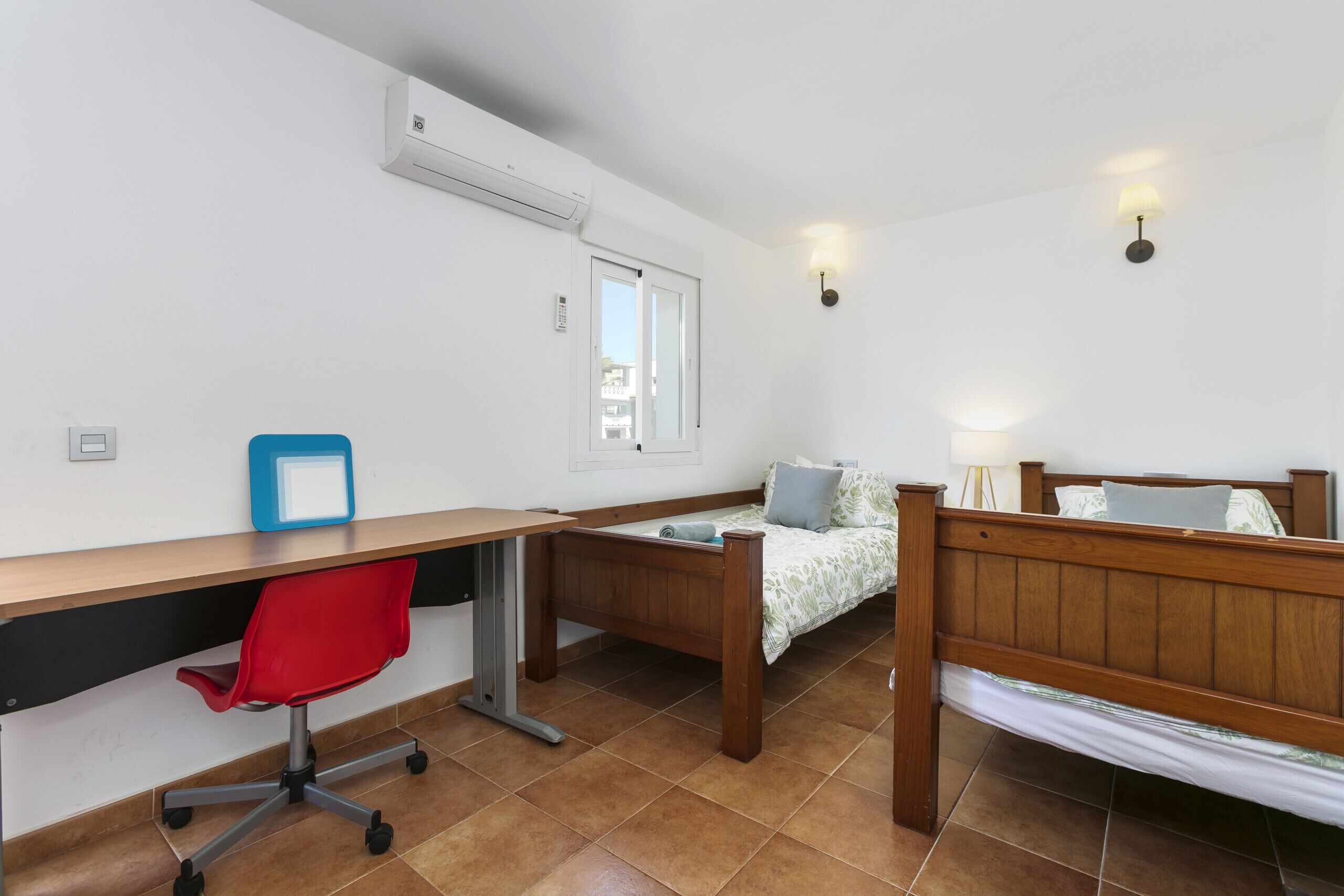 Un dormitorio con una cama de madera, un escritorio con una silla roja, una ventana y un aire acondicionado instalado en la pared.