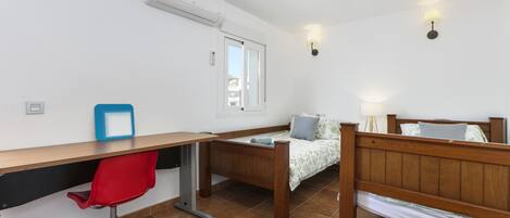 Un dormitorio con una cama de madera, un escritorio con una silla roja, una ventana y un aire acondicionado instalado en la pared.