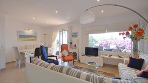 A modern living room with a sofa, chairs, a dining table, and a TV.