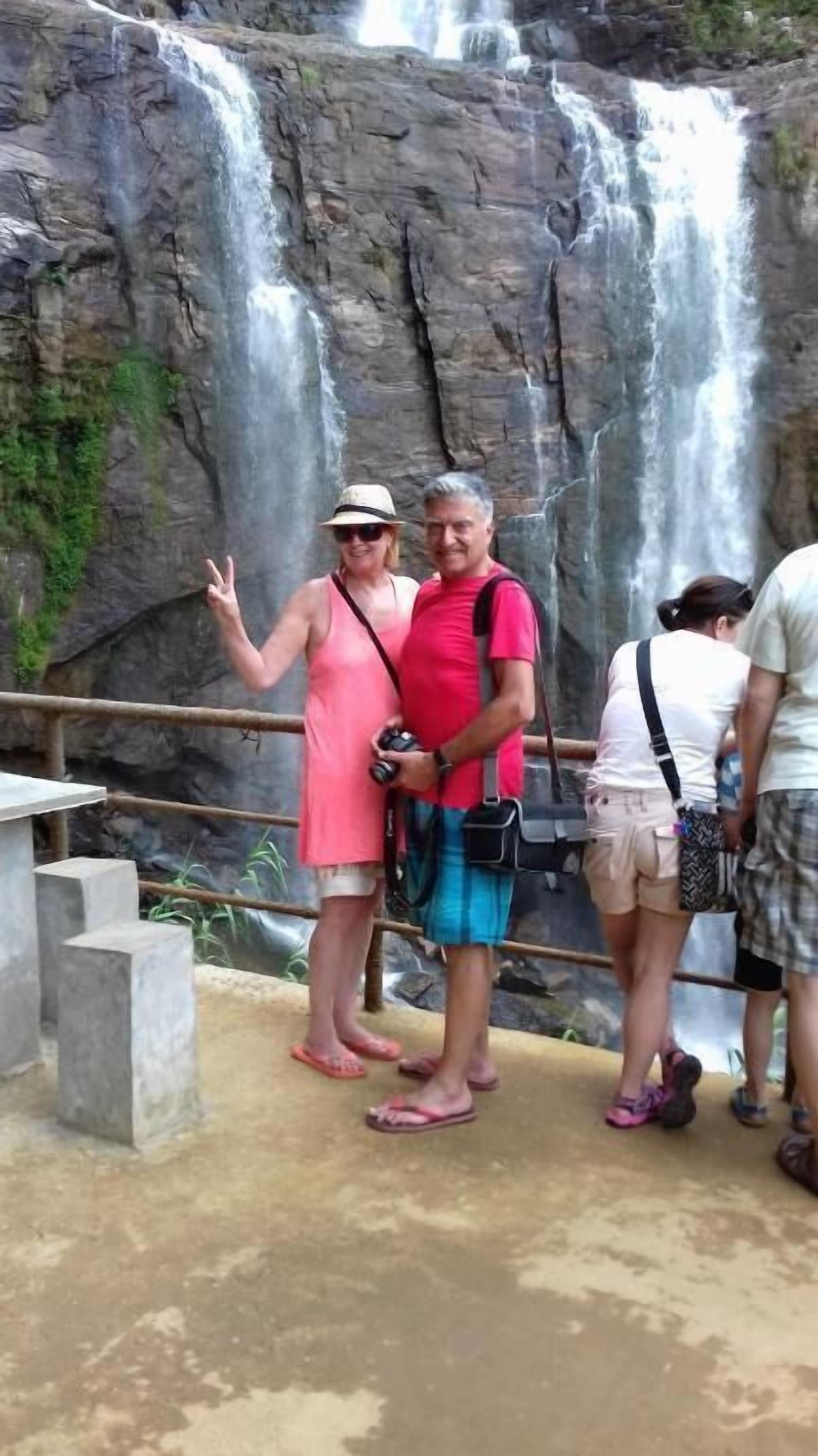 A group of people standing near a waterfall with a concrete viewing platform.